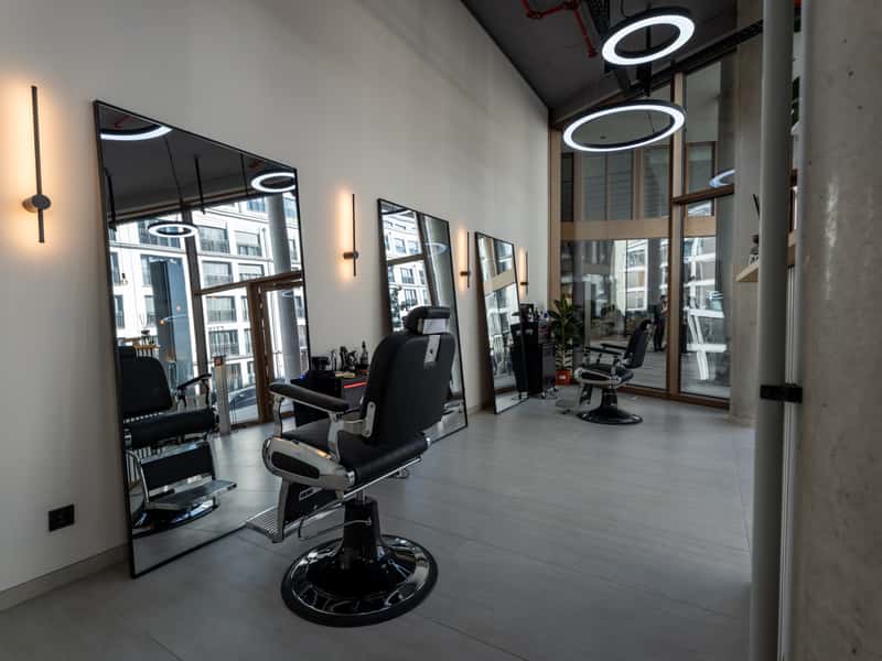 Barber-Bereich mit schwarzem Barberstuhl vor großen Wandspiegeln und warmen Wandleuchten