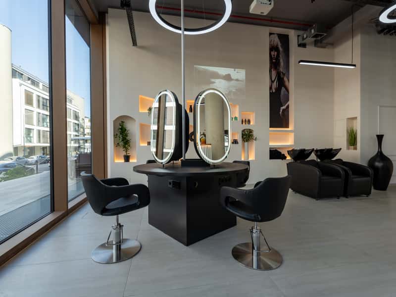 Styling-Insel mit zwei ovalen, beleuchteten Spiegeln, dahinter Waschplätze und Wandnischen mit Licht